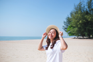 Portrait image of a beautiful woman holding hat while strolling on the beach