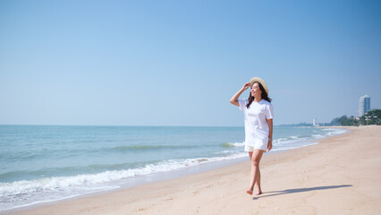 Portrait image of a young woman while strolling on the beach with the sea and blue sky background
