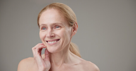 Real people - age, beauty, health and dry skin care concept - beautiful mature Caucasian middle aged woman in her 50s touching her face skin with a slight smile and good mood