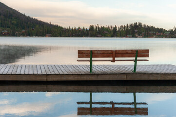 Empty bench on a misty lakeside dock at dawn