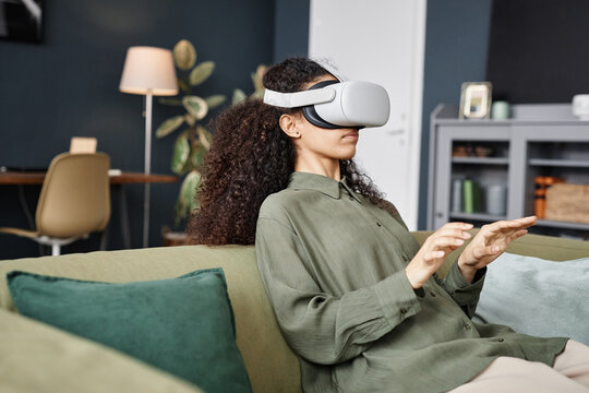 Medium shot of young biracial woman with curly hair wearing VR headset working online typing text in air, copy space