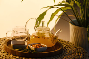A teapot with sea buckthorn tea, honey and a plate with sea buckthorn on a tray