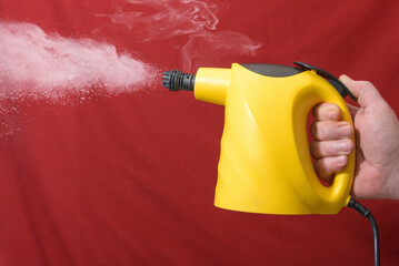 A person is holding a yellow steam cleaner with a red background