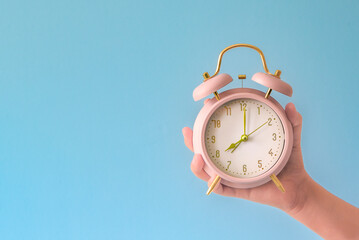 A hand holding a pink alarm clock with the time of 08.00