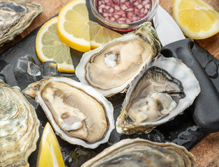 Opened raw oysters with sauce and lemon slices on gray stone serving board. Delicacy food. © volff