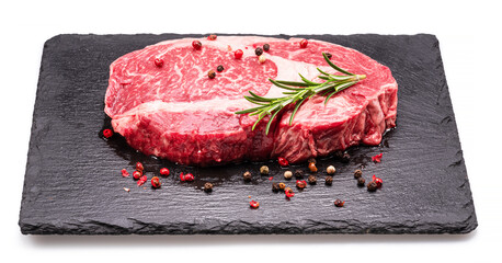 Raw ribeye steak with pepper corns and rosemary on graphite serving board isolated on white...