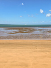 Calm beach at low tide with clear blue sky, yellow sand and a small white boat.