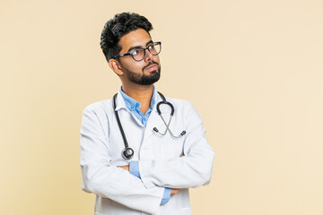 Portrait of happy Indian young doctor cardiologist man smiling, glad expression looking at camera, resting, relaxation feel satisfied good news. Arabian apothecary pharmacy guy on beige background