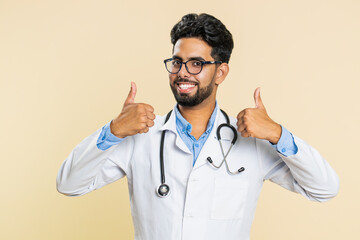 Like. Indian young doctor cardiologist man raises thumbs up agrees, gives positive reply good idea feedback, celebrating success victory. Arabian apothecary pharmacy guy isolated on beige background
