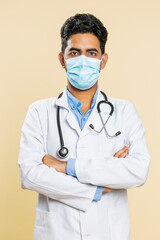 Indian doctor cardiologist man wearing medical mask on face protection from bronchitis asthma allergy flu pneumonia disease problem. Arabian apothecary pharmacy guy on beige background. Vertical