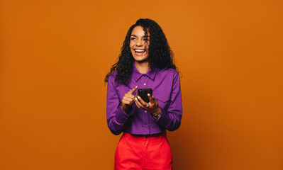 Vibrant woman smiling and browsing on a mobile phone against a cheerful orange background