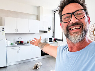 One man dow owner take selfie picture indoor inside house showing kitchen and background space. Happy mature male with beard and glasses smile at the camera and show home interior. Cheerful people