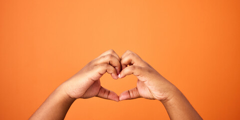 Love, hands and heart shape in studio for care, support and romance on orange background. Person,...