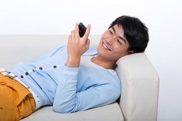 Shed young man lying on the sofa on your cell phone