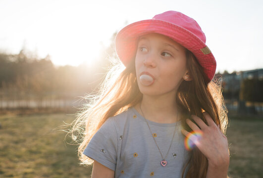 girl blowing bubbles with bubblegum in the garden at sunset
