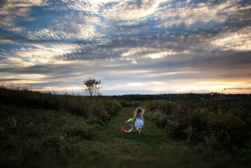 Little girl running in green field with streamer at sunset