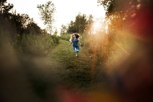 Beautiful little girl dancing in green field at sunset