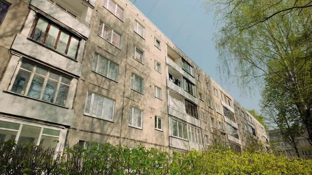 Aged ex soviet apartment block with windows in green spring landscape