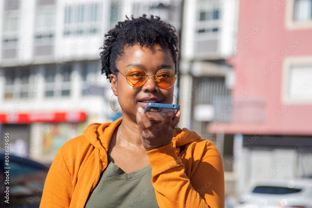 Wall mural afro woman sending a voice message with the phone on the street