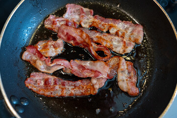 Frying bacon slices in frying pan on stove