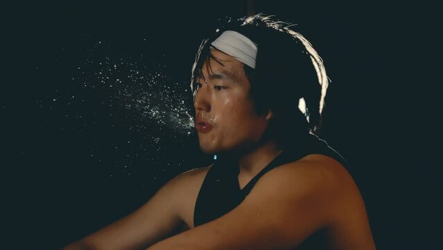 Asian male athlete spitting water in slow motion after hard workout in dark gym, backlit close up 4k 800fps