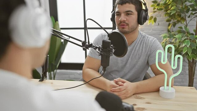 Two men engaged in a conversation at a modern podcasting studio, one speaking into a microphone.