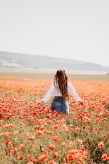 Woman poppies field. Back view of a happy woman with long hair in a poppy field and enjoying the beauty of nature in a warm summer day.