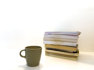 Coffee cup next to pile of books on white background. Creative photo.