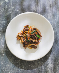 A plate of Korean fried beef and vegetables including carrots and greens garnished with sesame seeds served on a white plate on a textured gray surface.