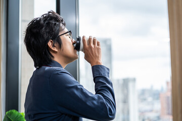 Exhausted Asain businessman drinking a cup of coffee in the office.