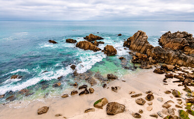 Panorama with picturesque rocks on sandy beach, surf and turquoise water on a cloudy day. Seen from a view point on famous 17 mile drive near Carmel. Pacific Grove Marine Gardens in California (USA).