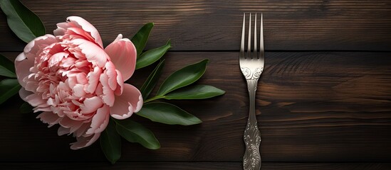 A peony flower rests elegantly on a wooden background surrounded by a fork knife and plate creating a visually appealing copy space image - Powered by Adobe