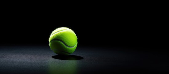 A tennis ball is lying on a black surface creating a simple and visually appealing image with space for text or other elements. Copy space image. Place for adding text and design