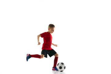 Little athlete boy, dribbling ball to take perfect goal against white studio background. Young football player in motion. Concept of professional sport, championship, youth league, hobby. Ad
