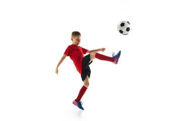 Naklejka premium Little sportive boy with soccer ball doing flying kick in motion against white studio background. Dynamic portrait. Concept of professional sport, championship, youth league, hobby. Ad