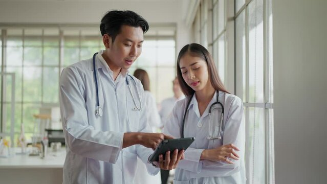 Asian male and female doctors using digital tablet, discussing patient diagnosis together in hospital. Two doctors using a digital tablet together in a medical office