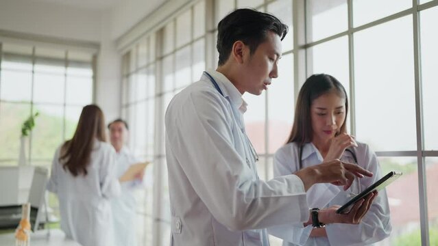 Asian male and female doctors using digital tablet, discussing patient diagnosis together in hospital. Two doctors using a digital tablet together in a medical office