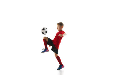Dynamic portrait of little sporty boy with soccer ball kicking ball with knee in motion against white studio background. Concept of professional sport, championship, youth league, hobby. Ad