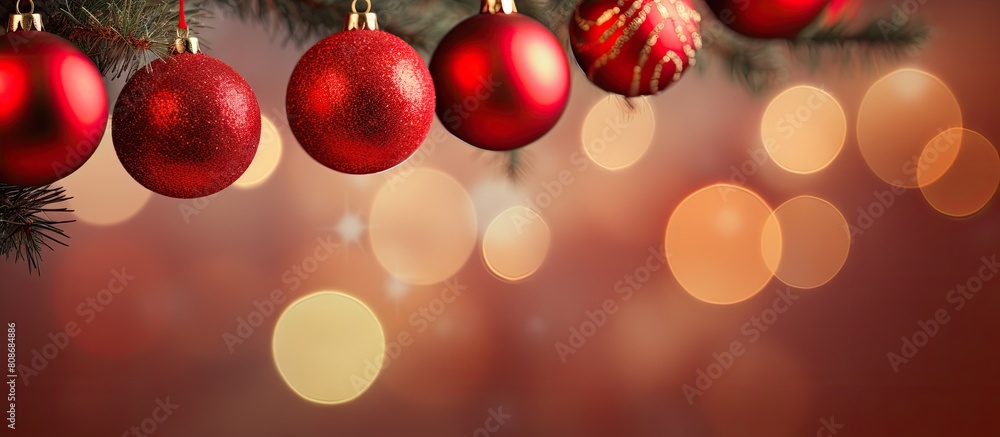 Poster Copy space image of red Christmas balls hanging on pine branches along with tree garland and ornaments against an abstract bokeh background