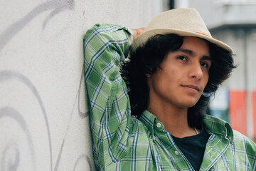 young latin hispanic man with hat posing on wall