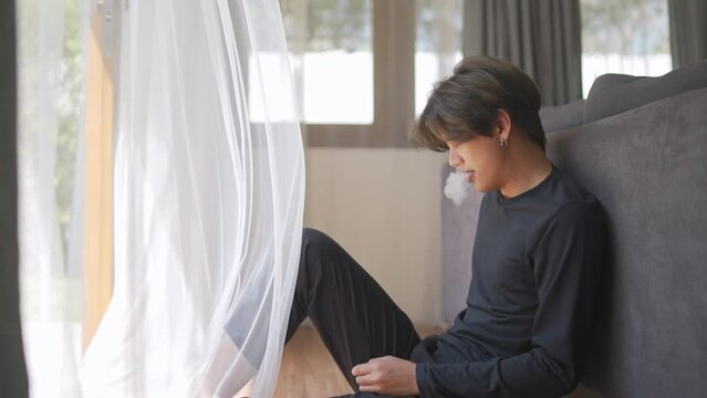 Depressed young Asian man sitting on the floor in living room with stressed and hopeless face. Loneliness sad guy being alone feeling bad and negative thinking. Mental health and life problem concept