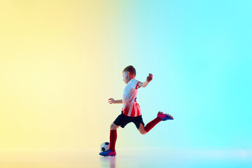 Boy kicking soccer ball in motion to take perfect pass in neon light against gradient background. Training exercises. Concept of professional sport, championship, youth league, hobby. Ad