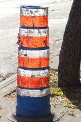 Reflective pole in orange, white, and blue hues near a tree
