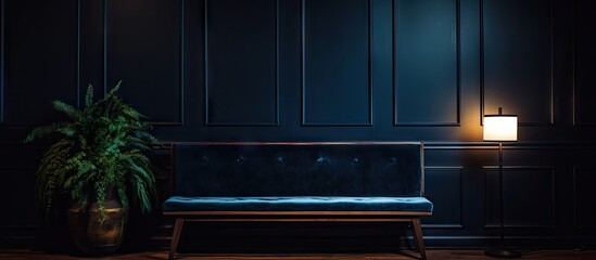 Image of a Navy blue velvet bench positioned alongside a table adorned with a potted plant sitting underneath a warm lamp within the interior of an anteroom. Copy space image