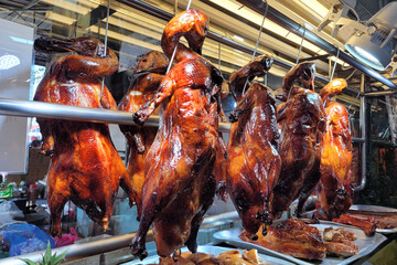 Roasted crispy ducks hanging from metal hooks in the window of a Chinese restaurant.