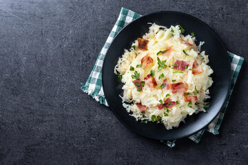 Slovak potato dumplings halusky with steamed sauerkraut and bacon on black background. Top view. Copy space