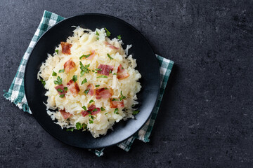 Slovak potato dumplings halusky with steamed sauerkraut and bacon on black background. Top view....
