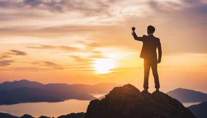silhouette of a businessman in a suit standing on a high mountain peak with one hand raised. 