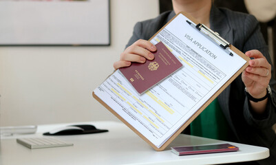 Close up of a woman holding a visa application paper document with a German passport laying on...