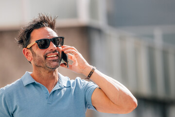 attractive young man in sunglasses talking on mobile phone on the street in summer outdoors